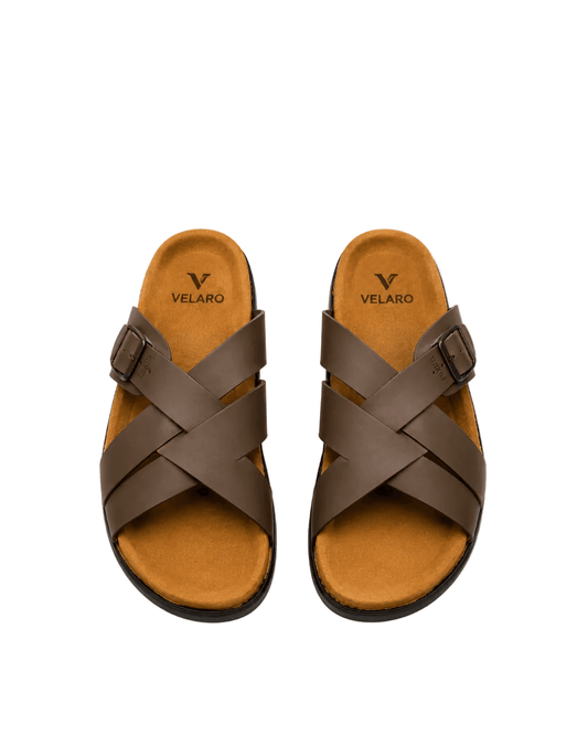 A pair of brown leather slide sandals with crisscrossing straps and adjustable side buckles, shown from a top-down view on a white background. The brand name 'VELARO' is printed on the tan footbed.